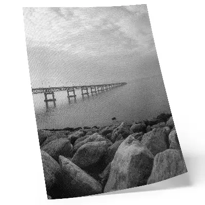 Poster friedliche Landschaft mit Brücke am felsigen Strand unter grauem Himmel
