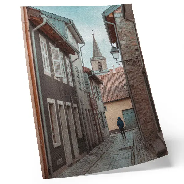 Poster enge Straße mit Mietshäusern, einem Turm und einer Person in einem blauen Mantel